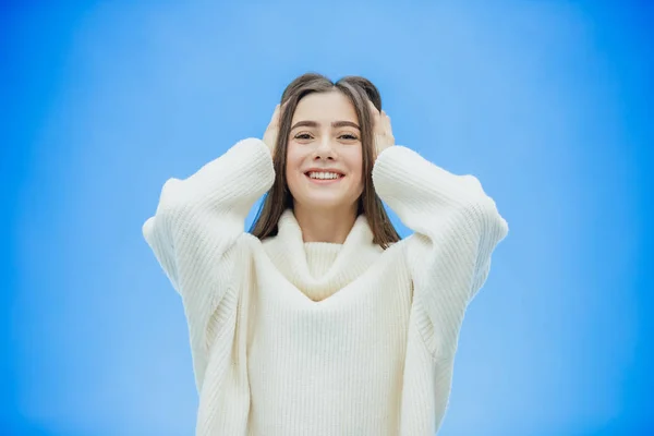 Μια νεαρή γυναίκα φοράει ένα πουλόβερ του χειμώνα σε ένα απομονωμένο γαλάζιο φόντο, χαμογελώντας στην αγάπη, υψώνοντας το χέρι από έκπληξη βάζει το κεφάλι της στο. — Φωτογραφία Αρχείου