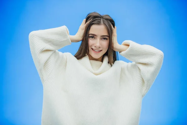 Egy fiatal nő visel egy téli pulóver egy elszigetelt kék háttér, mosolyogva, a szerelem, emeli a kezét fel a meglepetés helyezi a fejét. — Stock Fotó