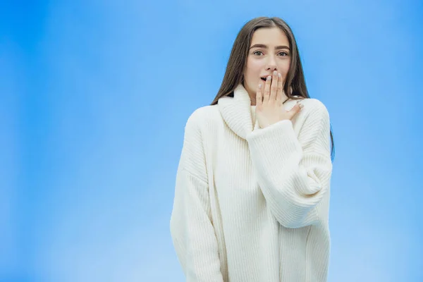 Una mujer joven lleva un suéter de invierno sobre un fondo azul aislado, sonriendo enamorada, levantando la mano de sorpresa pone la cabeza. Buena chica. . —  Fotos de Stock