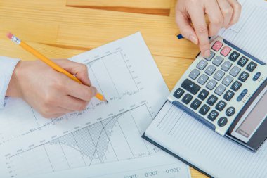 Bir akıllı telefon ve iş grafik üzerinde çalışan bir kadın işadamı close-up. Bir hesap makinesi kullanarak istatistiklerini hesaplama.