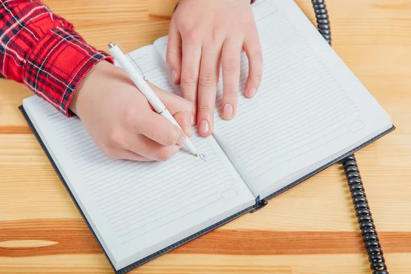 La fille est assez intelligente pour travailler au bureau. Pendant ce temps, il crée des étapes importantes pour la croissance de l'entreprise. Ecrire dans un carnet avec un stylo blanc . — Photo