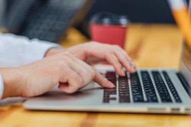 Bir dizüstü bilgisayar için çalışan bir kahve genç iş kız tutuyor. Bir dizüstü bilgisayar kullanarak bir modern iş kadından yaşam tarzı. Kadın el bir online web sitesi okuma üzerinde çalışıyoruz. İş kavramı. Bu sırada