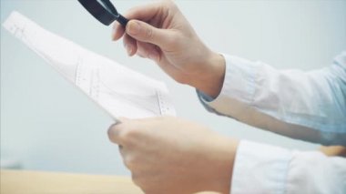 Genç işadamı büyüteç ile sayfaları istatistikleri ile arıyorum. Dikkatli bir şekilde her basamak gözden geçirme.