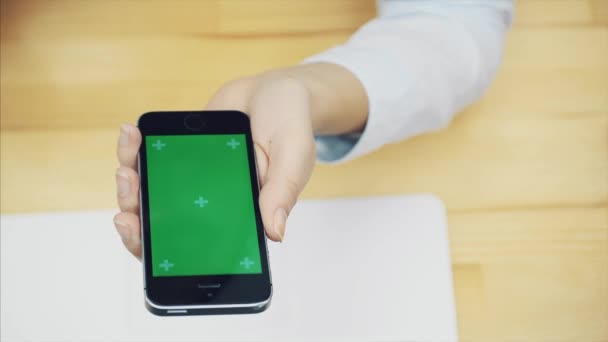 As mãos femininas tocam em um smartphone para usar um dispositivo para se comunicar. Na mesa do escritório com computadores e equipamentos. Tela verde na tela do smartphone. Espaço de cópia . — Vídeo de Stock