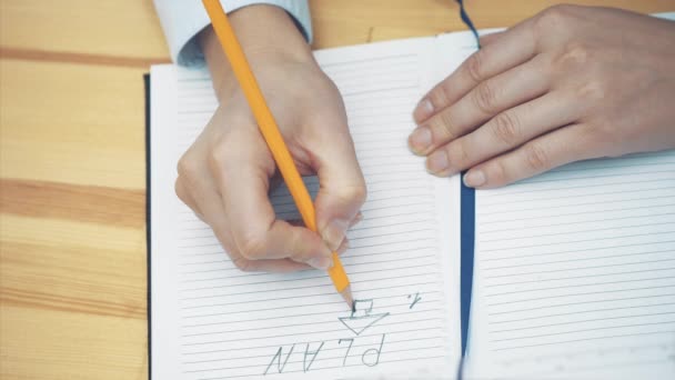 Close-up da mão feminina escrevendo estratégia no caderno com lápis. Mulher de negócios a inventar um novo plano de negócios. Estratégia e conceito de planeamento — Vídeo de Stock
