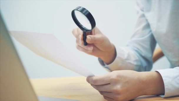 Jeune homme d'affaires avec loupe, regardant des feuilles avec des statistiques. Examen attentif de chaque chiffre . — Video