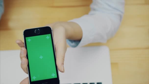 Female hands touch a smartphone to use a device for communicating on the office desk with computers and equipment, a green screen on the smartphone screen, copy space. — Stock Video