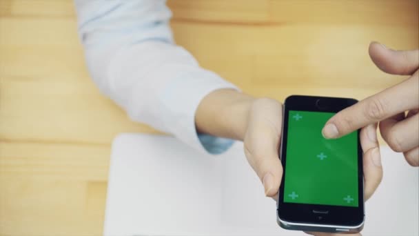 As mãos femininas tocam em um smartphone para usar um dispositivo para se comunicar na mesa do escritório com computadores e equipamentos, uma tela verde na tela do smartphone, espaço de cópia . — Vídeo de Stock