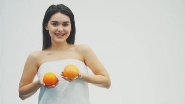 Genç güzel kız beyaz bir arka plan üzerinde ayakta. Portakal elinde tutar ve kameraya benziyor. Güzel siyah uzun saçları var..