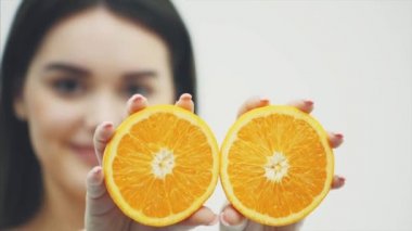 Mutlu genç kız meyve ile poz. Beyaz bir arka plan üzerinde elinde bir portakal parçaları close-up. İki adet meyve tutan onun silah çene düzeyini kaldırma.