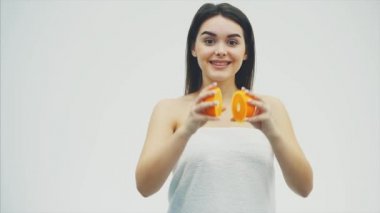 Mutlu genç kız meyve ile poz veriyor. Bu sırada kameraya bakıyor. İki adet turuncu elleri ve gülümsüyor tutar.