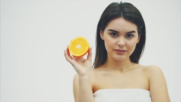 Joven hermosa joven modelo de moda con una rebanada de naranja sobre un fondo blanco. Con maquillaje y hermoso pelo largo negro . — Vídeos de Stock