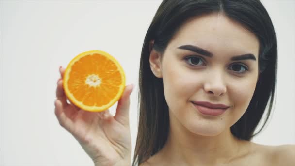 Junge schöne junge Mädchen-Mode-Modell mit einem Stück Orange auf weißem Hintergrund. mit Make-up und schönen schwarzen langen Haaren. — Stockvideo
