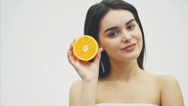 Giovane bella ragazza modello di moda con una fetta di arancione su uno sfondo bianco. Con trucco e bei capelli lunghi neri . — Video Stock