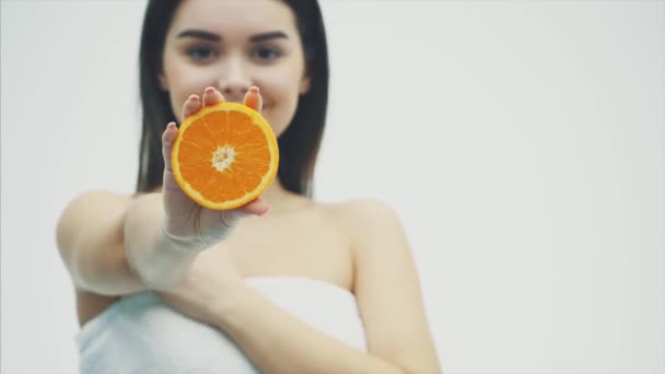 Jeune jolie fille debout sur un fond blanc. En même temps, tenant la moitié d'une orange dans ses mains. Fond flou . — Video