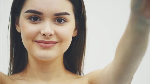 Chica joven y feliz posando con frutas. El primer plano de los fragmentos anaranjados en las manos sobre el fondo blanco. Levantando sus brazos al nivel de la barbilla sostiene dos pedazos de fruta . — Vídeos de Stock