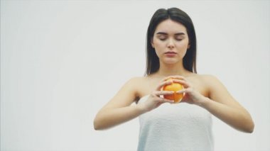 Genç güzel kız beyaz bir arka plan üzerinde ayakta. Bu sırada, gerildi portakal Kapalı gözlerle kaplıdır. Bir süre sonra o onun gözlerini açar ve farklı yönlere ellerini tatili.