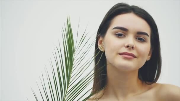 Jonge mooie lachende model met natuurlijke make-up, lange wimpers en groene blad van varens. Spa, huidverzorging en wellness. — Stockvideo