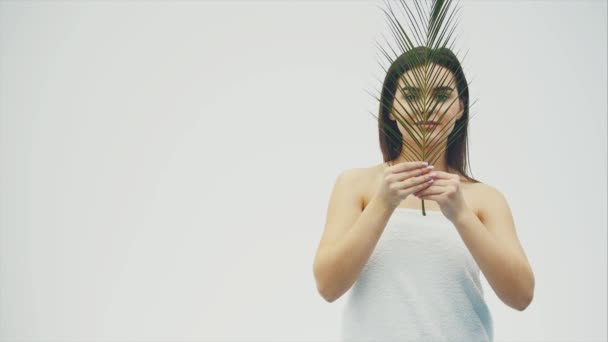 Портрет красивой молодой женщины с натуральным макияжем и тропическим листом на белом фоне . — стоковое видео
