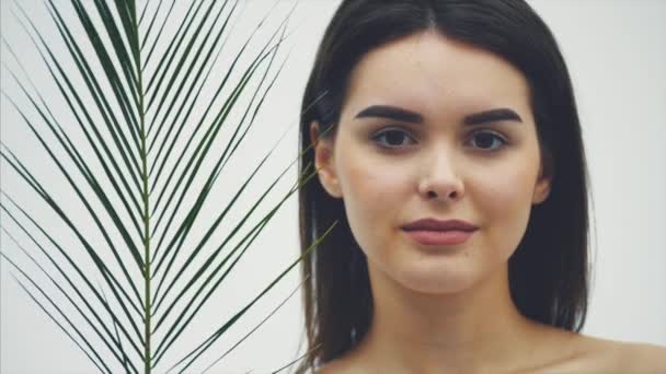 Unga vackra leende modell med naturlig makeup, långa ögonfransar och grönt blad av ormbunkar. Spa, hudvård och friskvård. — Stockvideo