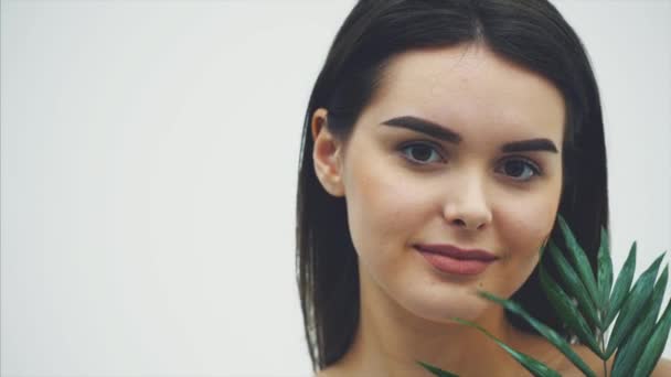 Belle jeune femme avec une peau parfaite et un maquillage naturel posant devant une plante. Feuilles vert tropical fond de fougère. SPA, bien-être, soins du corps et soins de la peau . — Video