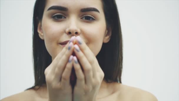 Elegance a něhy. Krásná mladá brunetka vlasy žena fouká lístků na zemi. Při pohledu na fotoaparát, stoje izolovaných na bílém a usmívá se. — Stock video