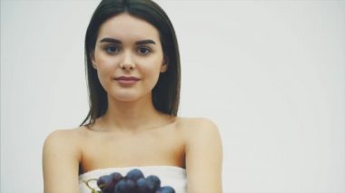 Güzel bir ince kız sağlıklı meyve yiyor. Bu sırada, genç ve güzel bir kadın olgun bir üzüm buket onun elinde yükselir. Bu süre içinde o beyaz bir arka plan üzerinde duran ve bakarak