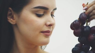 Güzel bir ince kız sağlıklı meyve yiyor. Olgun bir üzüm buket ve bir gerçek tutan genç ve güzel bir kadın portresi.