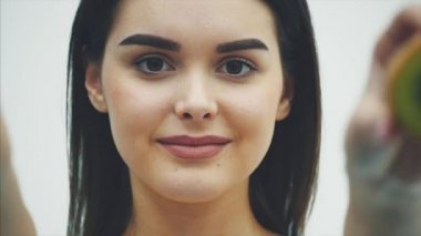 Genç güzel kız beyaz bir arka plan üzerinde ayakta. Bu sırada, kivi parçacıklar open-eyed, onları gösteren göz düzeyinde tutulur.