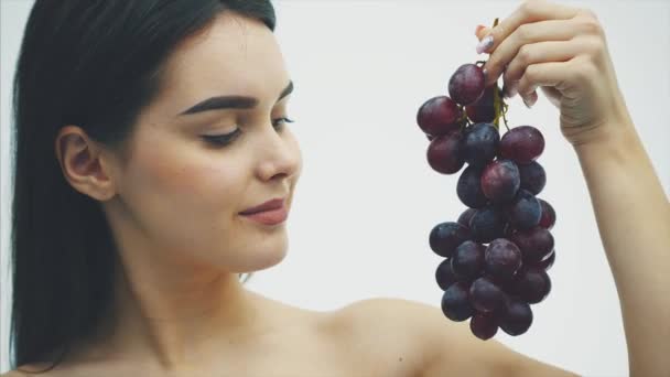 Uma menina bonita e magra come frutas saudáveis. Retrato de uma jovem bonita segurando um buquê de uva madura e uma verdade . — Vídeo de Stock
