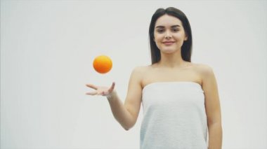 Beyaz bir arka plan üzerinde duran genç, oldukça neşeli bir kız. Bu süre içinde mandalina katlanıyor ve kısmen fotoğraf makinesine benziyor. Bir güzel temiz tenli ve uzun siyah saçlı.