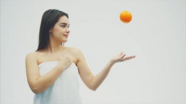 Beyaz bir arka plan üzerinde duran genç, oldukça neşeli bir kız. Bu süre içinde mandalina katlanıyor ve kısmen fotoğraf makinesine benziyor. Bir güzel temiz tenli ve uzun siyah saçlı.