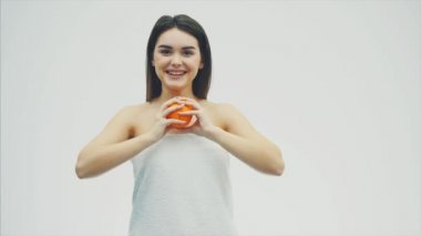 Mutlu genç kız meyve ile poz veriyor. Bu sırada kameraya bakıyor. İki adet turuncu elleri ve gülümsüyor tutar. Beyaz arka plan.