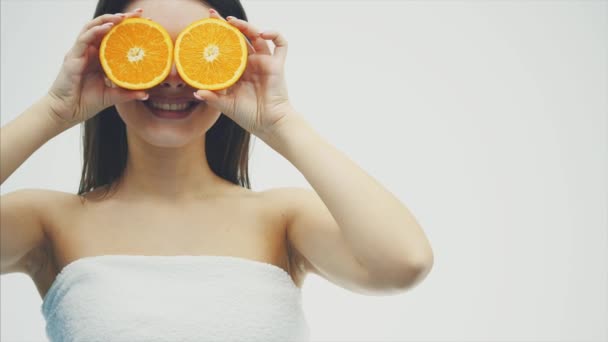 Potret indah seorang wanita muda yang cantik berpose dengan buah oranye terisolasi di atas latar belakang putih. Menutup matanya . — Stok Video