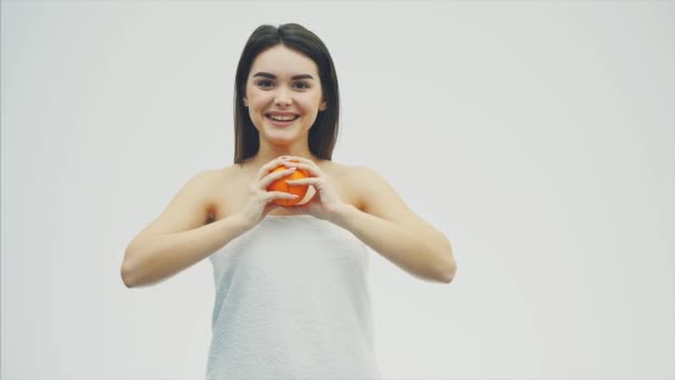 Jovem feliz posa com frutas. Durante isso, ela olha para a câmera. Tem dois pedaços de laranja nas mãos e sorri. Fundo branco . — Vídeo de Stock