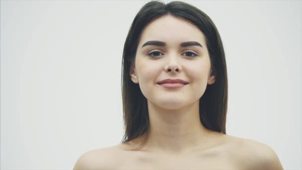 Retrato de uma bela jovem de pé olhando para a câmera. Cuida do seu corpo usando frutas e fazendo máscaras. Segurando uma meia fruta laranja em seus ombros com longos cabelos pretos, isolado em — Vídeo de Stock