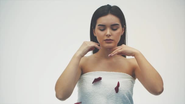 Hermosa chica morena en su belleza. Maquillaje dorado de noche y lápiz labial rojo con cabello oscuro sobre fondo blanco. los pétalos de rosas rojas volando hasta su cara . — Vídeos de Stock