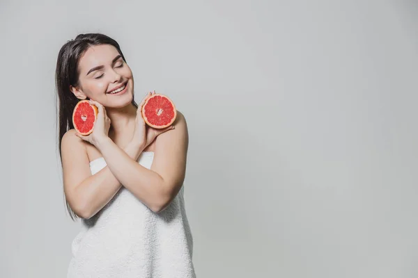 Chica joven y feliz posando con fruta. Rodajas de pomelo rojo en sus manos sobre un fondo blanco. Levantando los brazos al revés, los cruzaron . — Foto de Stock