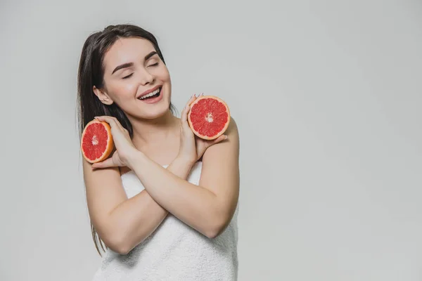 Menina feliz posando com frutas. Fatias de toranja vermelha em suas mãos sobre um fundo branco. Levantando os braços de cabeça para baixo, cruzaram-nos. . — Fotografia de Stock