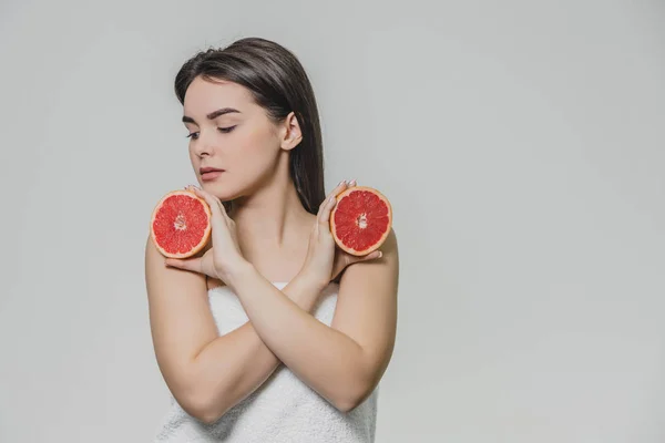 Chica joven y feliz posando con fruta. Rodajas de pomelo rojo en sus manos sobre un fondo blanco. Levantando los brazos al revés, los cruzaron . — Foto de Stock