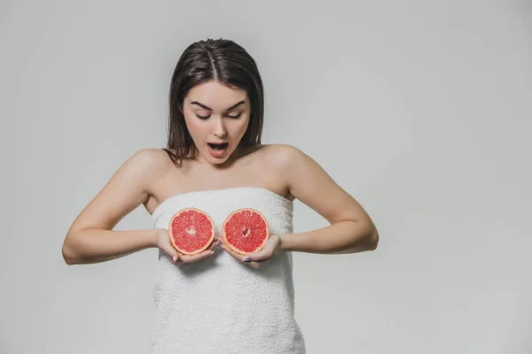 Chica joven y feliz posando con fruta. Rodajas de pomelo rojo en sus manos sobre un fondo blanco. Levantando sus brazos al nivel del pecho sostiene dos pedazos de fruta . — Foto de Stock