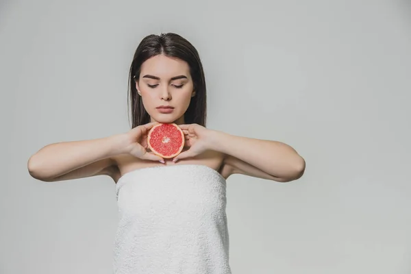 Una joven feliz posa con fruta. Durante este tiempo, ella sostiene un trozo de pomelo en su cuello con ambas manos . — Foto de Stock