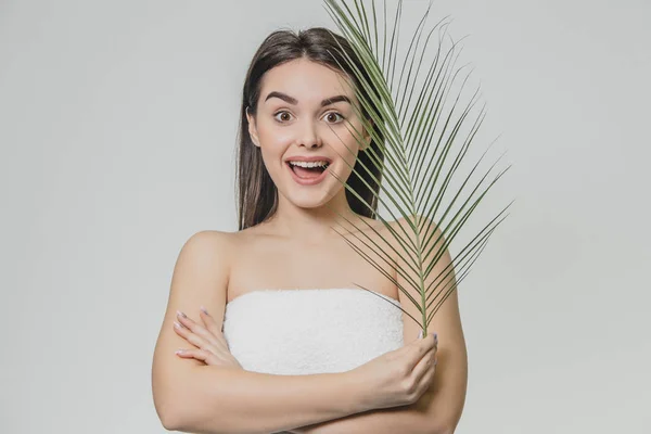 The face is a beautiful young woman with clean, perfect skin, covered with leaves. Portrait of a beauty model with natural naked makeup and long eyelashes. Spa, skin care and wellness.