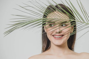 Çekici bir mutlu kız geniş gülümsüyor ve yüzü güneş eğreltiotu yaprakları ile yarısı kapsar. Yeşil, sağlıklı cilt ve çevre dostu kavramı.