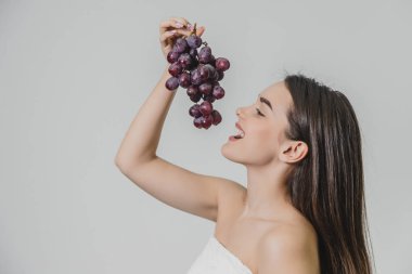 Güzel genç esmer kız mutlu bir gülümseme ile. Taze üzüm elinde taşıyan, beyaz bir arka plan üzerinde izole. Yandan görüntülemek.