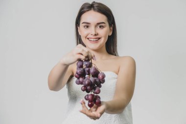 Güzel genç esmer kız mutlu bir gülümseme ile. Taze üzüm demet elinde tutarak, beyaz bir arka plan üzerinde izole.