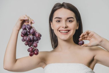 Güzel genç esmer kız mutlu bir gülümseme ile. Taze üzüm demet elinde tutarak, beyaz bir arka plan üzerinde izole.