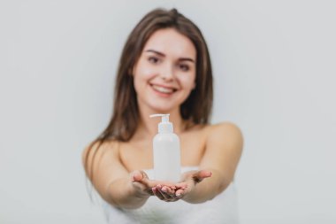 Model bakmak - bu güzel bir genç tek kişilik bir beyaz terry havlu içinde olduğunu. Omuz ve beyaz bir arka plan üzerinde dururken gülümseyen bir vücut losyonu uygulayın.