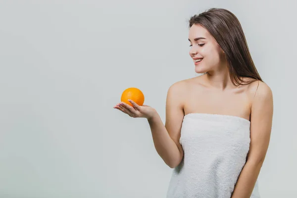 Retrato de una linda joven atractiva mujer de medio ojo sosteniendo una naranja en sus manos y mirando a una naranja, aislada sobre un fondo blanco . — Foto de Stock