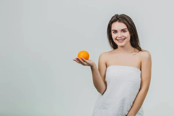 Retrato de una guapa y atractiva media mujer sosteniendo una naranja en sus manos y mirando a la cámara, aislada sobre un fondo blanco . — Foto de Stock